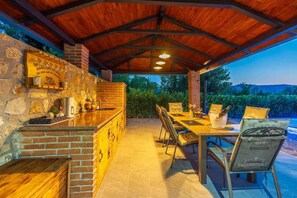 Um pátio externo com churrasqueira de tijolo, uma mesa com cadeiras e vista para a paisagem.