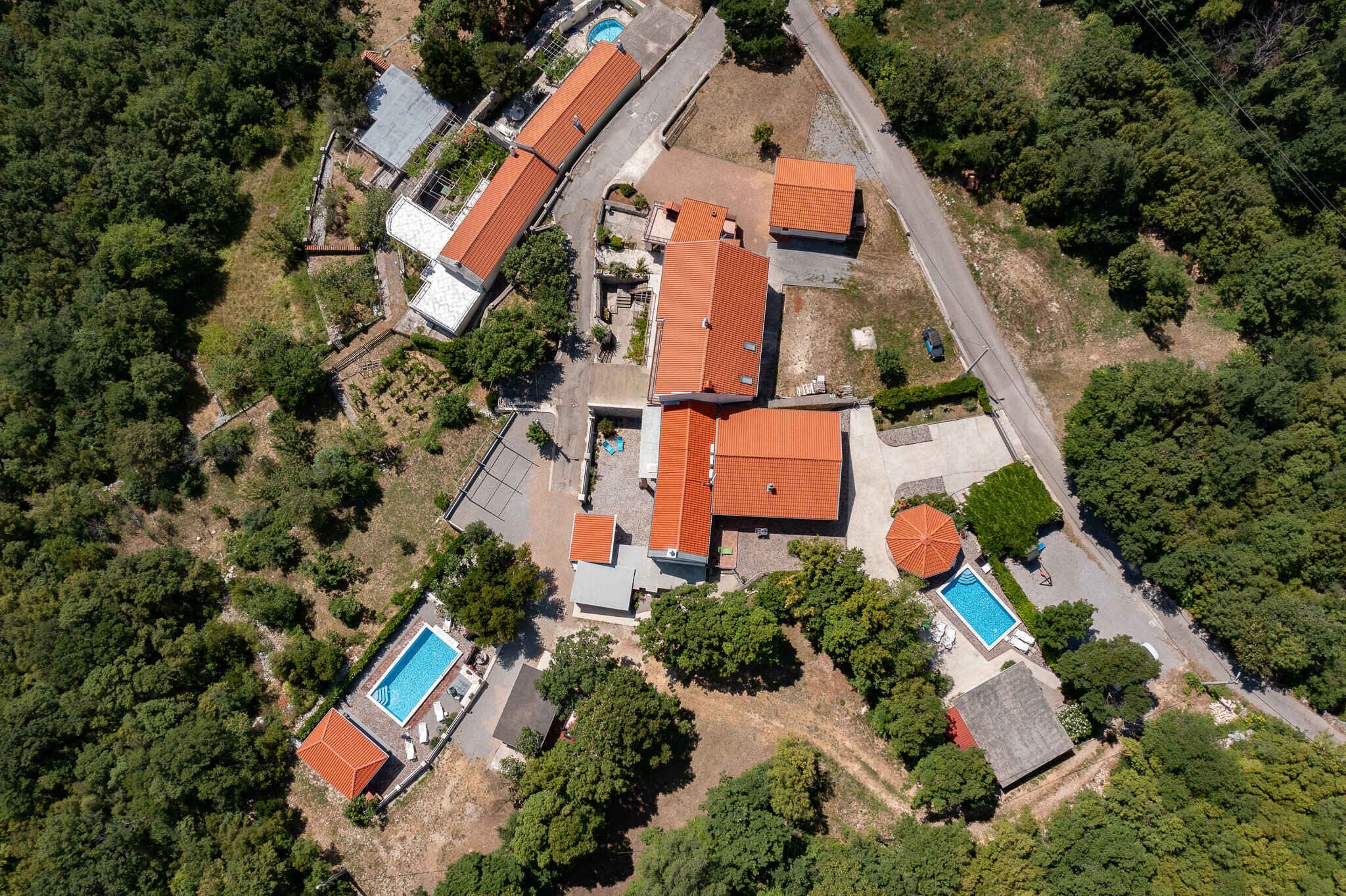 An aerial view of a residential property with multiple buildings, a swimming pool, and surrounding greenery.