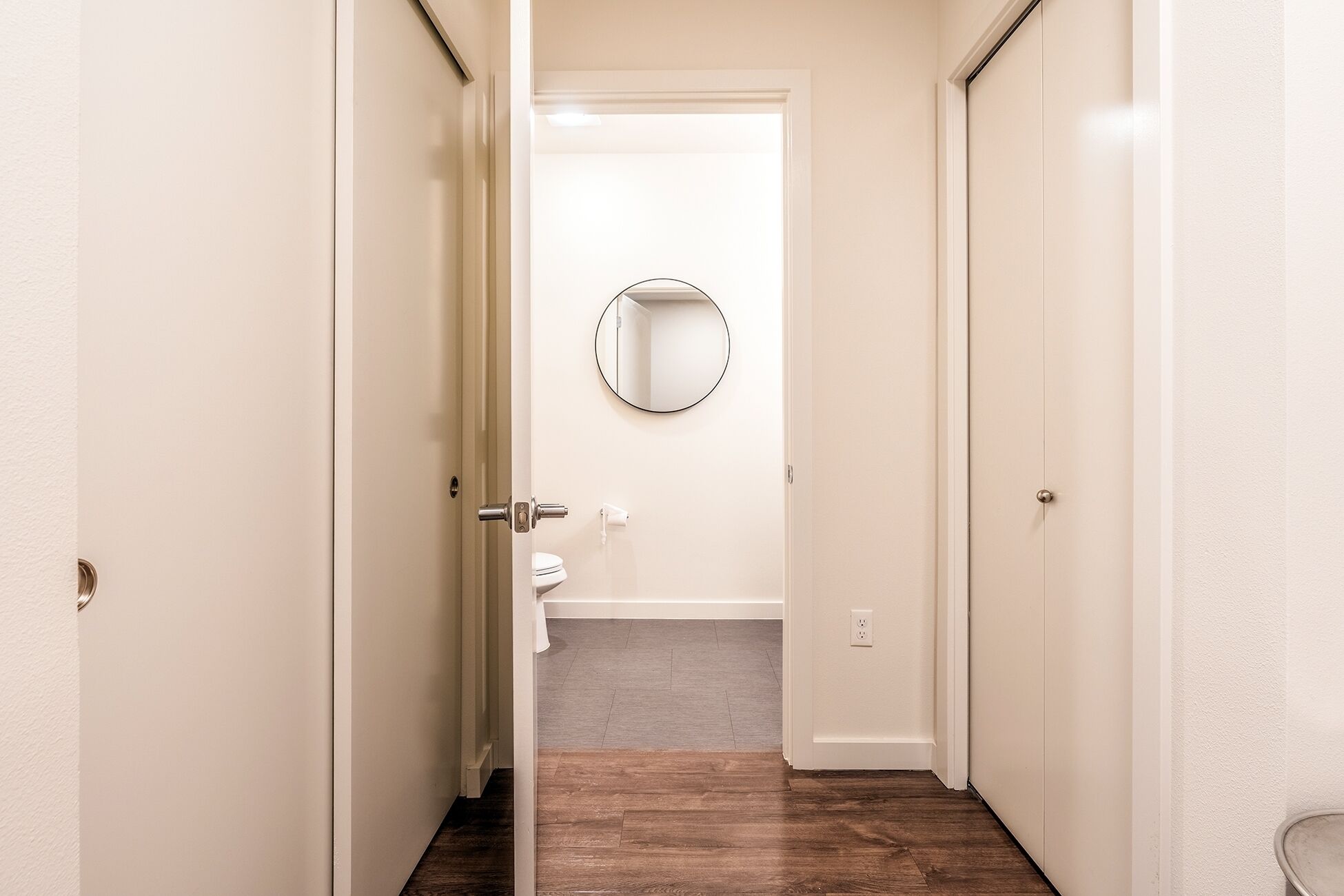 Passadís que condueix a un bany amb un vàter, un mirall i una porta blanca.