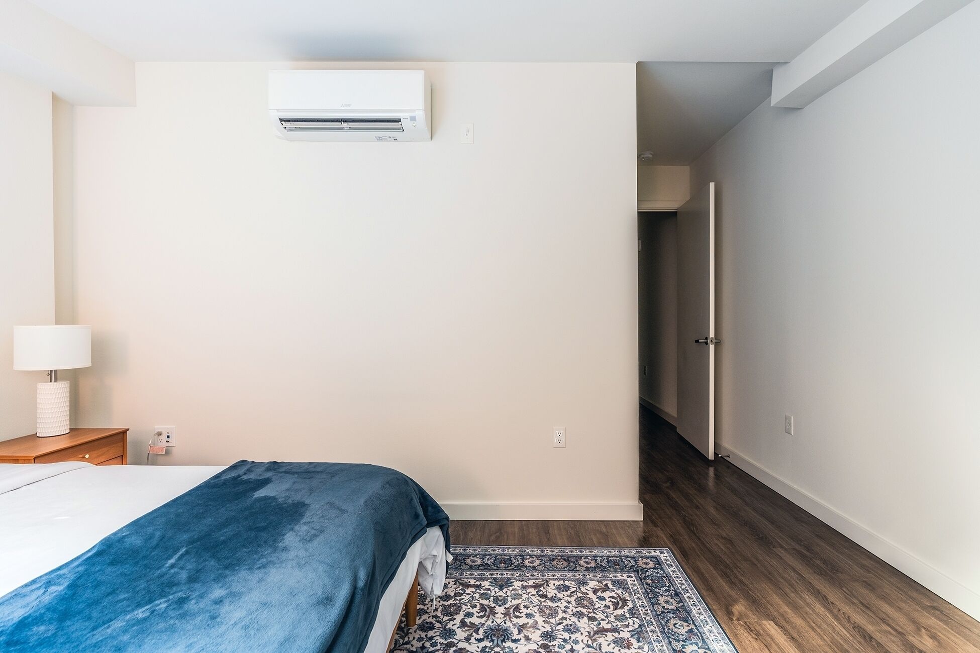 Een slaapkamer met een bed, een bedlamp, een kamerbreed tapijt en een airconditioning aan de muur.