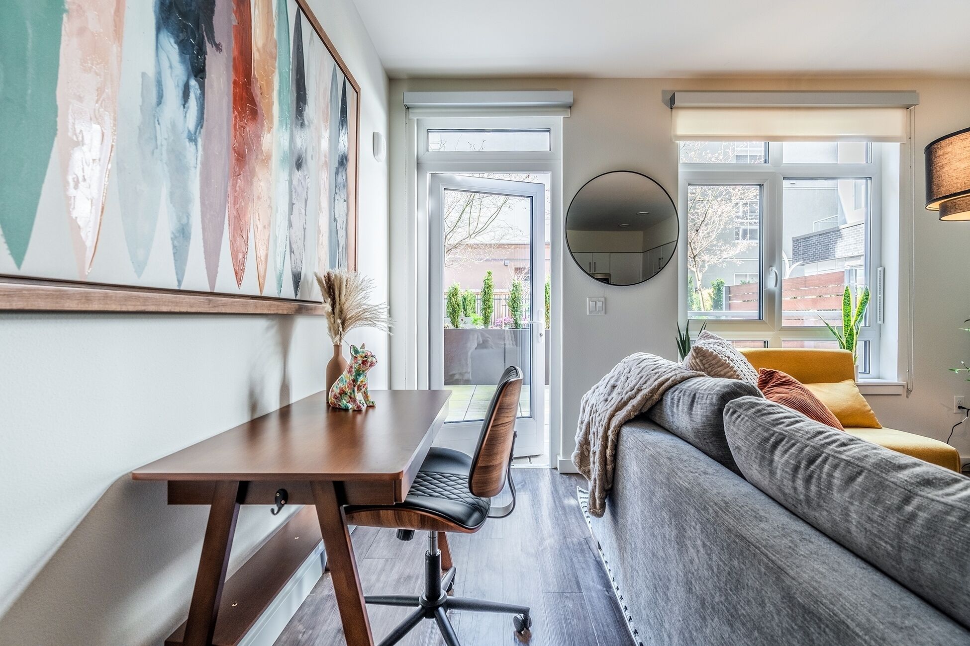 Una sala de estar moderna con un sofá, un escritorio y una silla. Se ve una ventana grande con vistas al exterior.