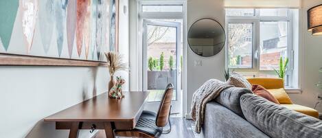 Una sala de estar moderna con un sofá, un escritorio y una silla. Se ve una ventana grande con vistas al exterior.