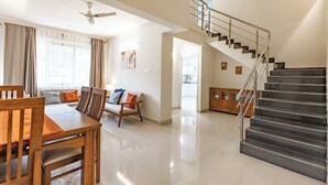 A spacious living area with a dining table, chairs, a sofa, and a staircase. - Elegant 2-Bedroom Duplex Apartment With 3 AC's In The Heart Of Benaulim (Benaulim)