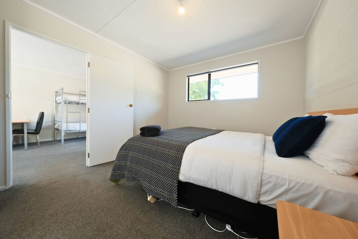 A bedroom with a bunk bed, a desk, a chair, a window, and a door.