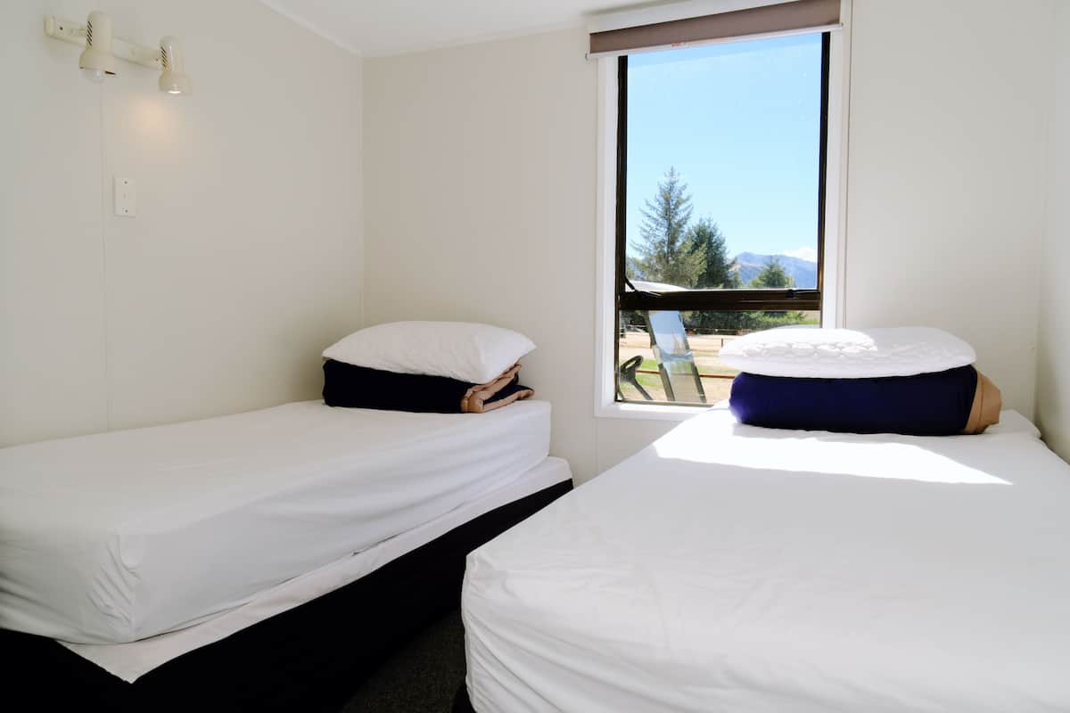 A room with two single beds, a window with a view of trees and mountains, and a wall-mounted light fixture.