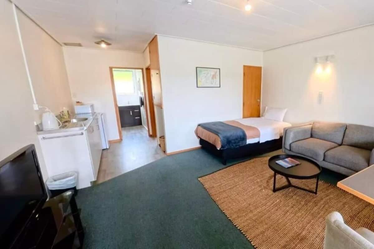 A compact hotel room with a bed, a sofa, a small table, and a kitchenette.