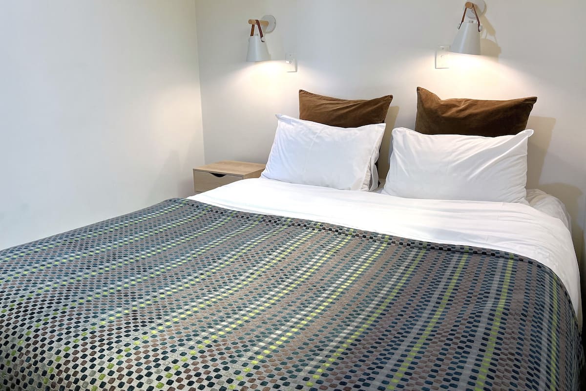 A bed with a patterned bedspread, two white pillows, and two brown pillows. There are two bedside tables with lamps.