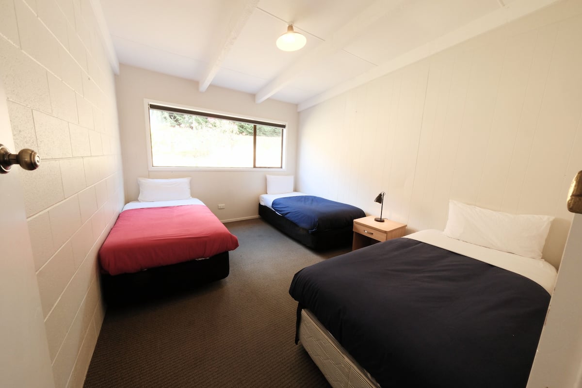 A small, well-lit room with two beds, a window, and a door.