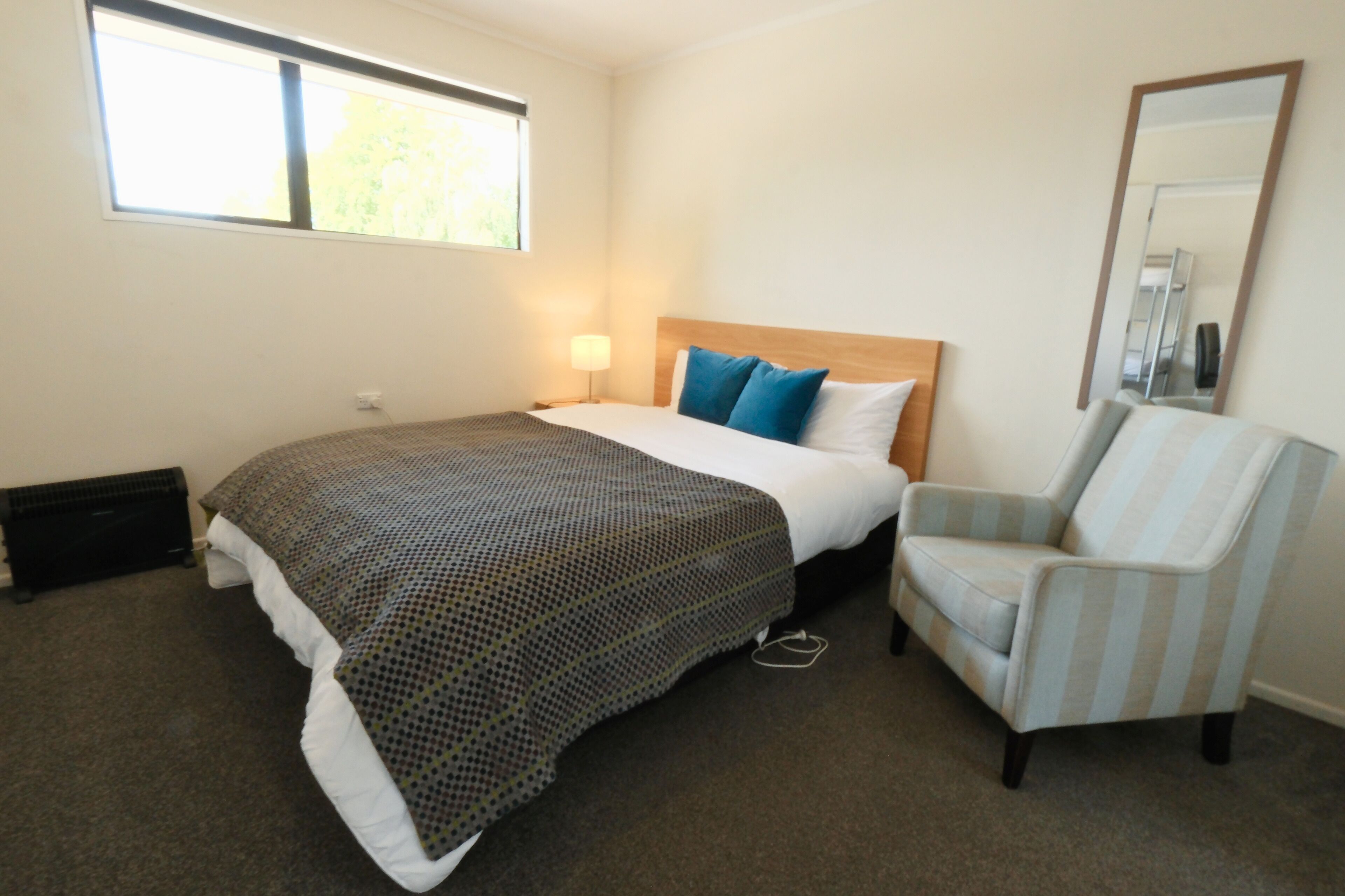 A hotel room with a bed, a chair, a window, and a mirror.