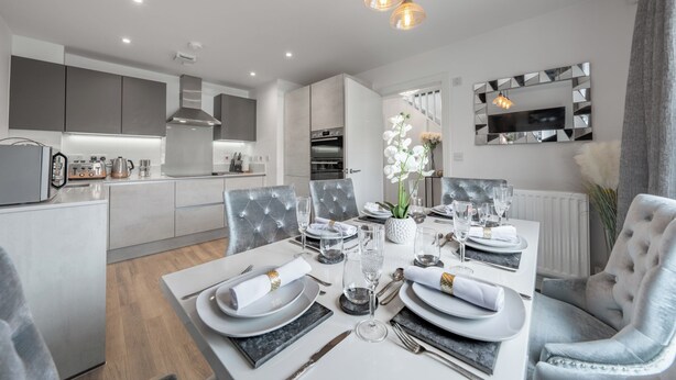 Un comedor moderno con una mesa blanca para cuatro personas, sillas tapizadas en gris y un sofá de color gris.