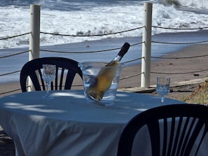 Ein Tisch mit einer Flasche in einem Glasbehälter, zwei leere Gläser und Blick auf das Meer.