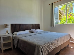 Une chambre à coucher avec un lit, une table de chevet, une lampe et une fenêtre donnant sur un paysage verdoyant.