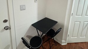 A small room with a white door, a white wall, a black table with two chairs, and an air conditioning unit mounted on the wall. - Room, cozy and well-lit (Tampa)