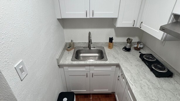 A compact kitchen with white cabinets, a stainless steel sink, a coffee maker, and a trash bin. - Room, cozy and well-lit (Tampa)
