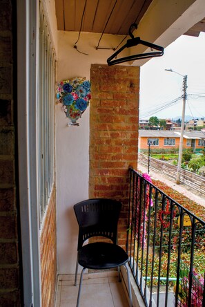 Un balcón con una silla, un perchero colgante y un arreglo floral decorativo.