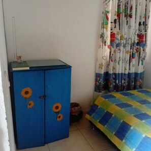 A bedroom with a blue wardrobe, a bed with a multicolored quilt, and a curtain with cartoon characters.