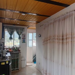 Una cocina con techo de madera, una ventana con cortina y una puerta que da a otra habitación.