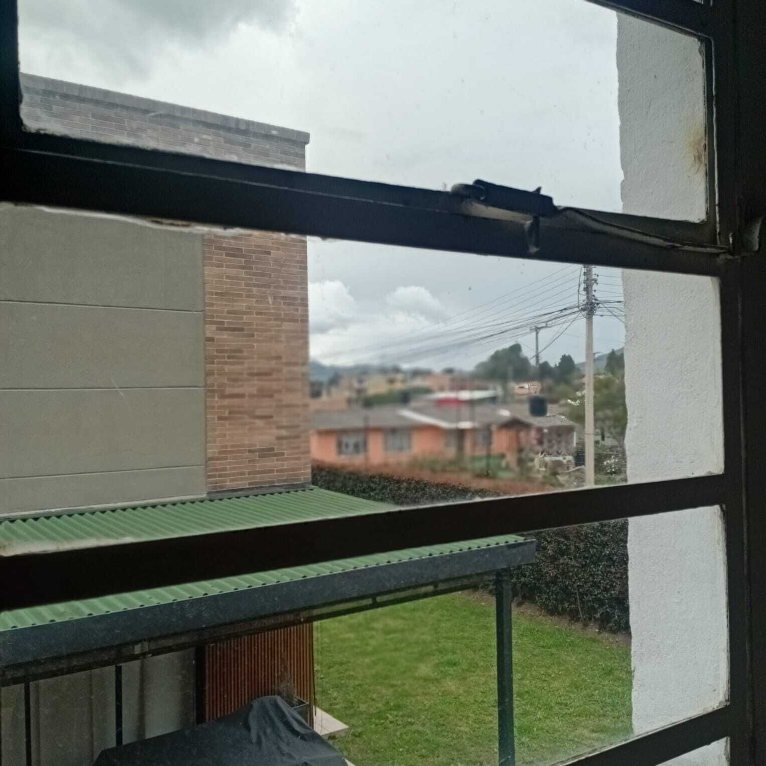 Janela com vista para uma área residencial, um muro de tijolos e um telhado verde.