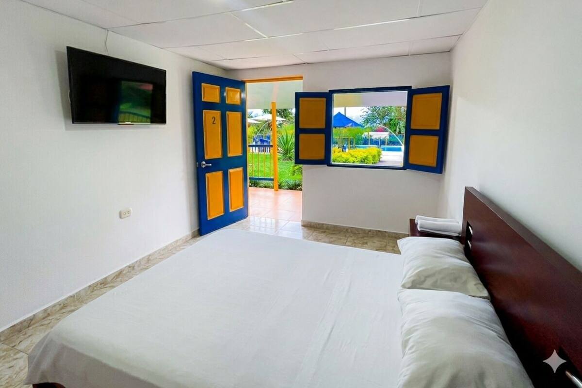 Une chambre avec un lit, un téléviseur fixé au mur et une porte donnant sur un espace extérieur.