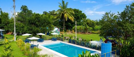 A swimming pool surrounded by greenery, a covered seating area, and a small pavilion.