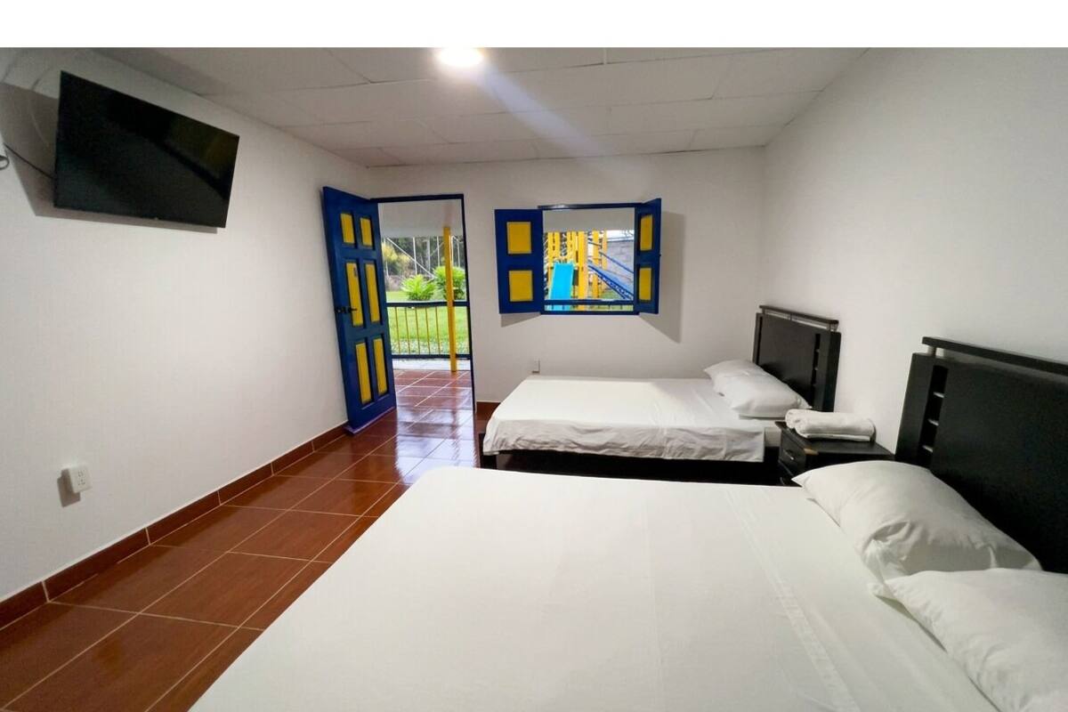 Une chambre avec deux lits, une télévision et une fenêtre donnant sur un terrain de jeux extérieur.