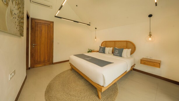 A bedroom with a wooden bed, a round rug, a wall-mounted nightstand, and a ceiling light fixture. - Premier Umalas Seminyak (Keroboken Kelod)