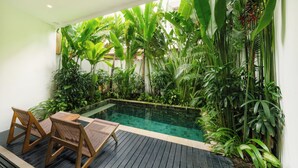 A pool area with wooden deck chairs, surrounded by lush tropical plants. - Premier Umalas Seminyak (Keroboken Kelod)