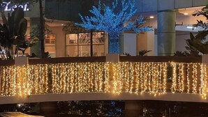 Un bâtiment à plusieurs niveaux agrémenté d’un élément aquatique, de guirlandes lumineuses et d’un arbre décoré de lumières bleues.