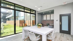 Ein modernes Interieur mit einem weißen Esstisch, grauen Stühlen, einem großen Fenster und einem Ausgangsschild.