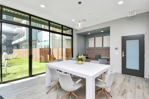 Ein modernes Interieur mit einem weißen Esstisch, grauen Stühlen, einem großen Fenster und einem Ausgangsschild.