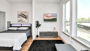 Ein modernes Schlafzimmer mit Bett, Nachttischen, einer Topfpflanze und einem großen Fenster.