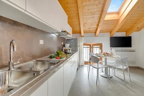 A modern kitchen with a wooden ceiling, a dining area with a table and chairs, and a TV mounted on the wall. - Residenza Lugana Pool & Garden in Peschiera Apt 6, Peschiera del Garda, Italy (Peschiera del Garda)