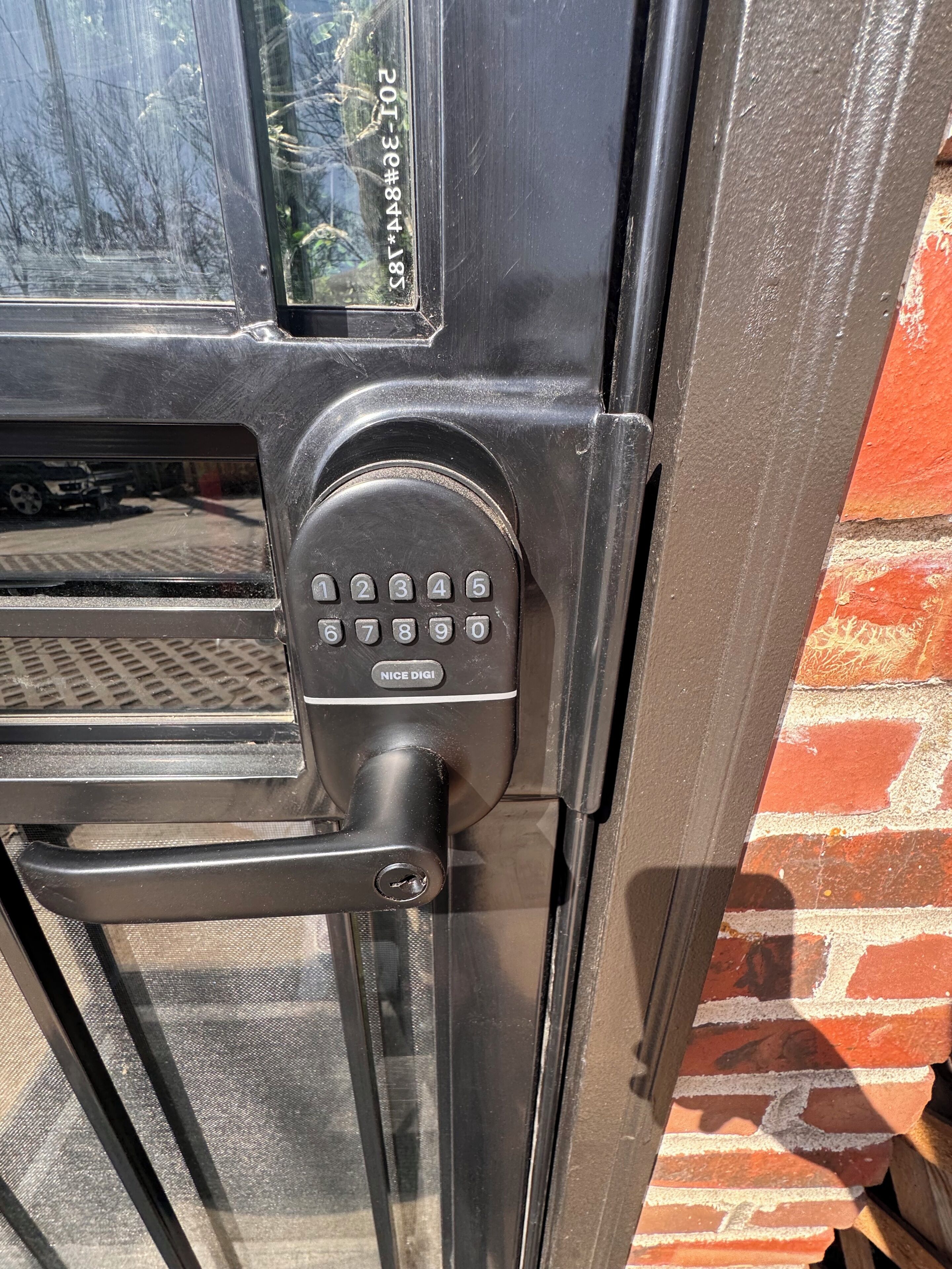 Una puerta con cerradura electrónica, una ventana con vistas a árboles y una pared de ladrillo.