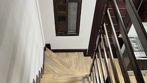 Una escalera de madera con barandilla que lleva a un cuarto con piso de baldosas y una ventana.