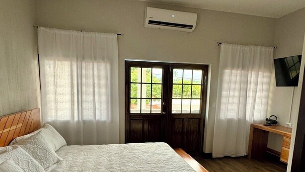 Un dormitorio con una cama grande, un cabecero de madera, un escritorio con una silla, un televisor y una ventana con cortinas.