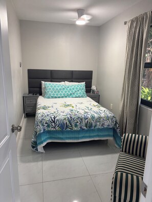 A bedroom with a bed, a nightstand, a chair, and a window with curtains. - Modern Luxury Apartment for Rent | Fully Furnished   (Naples)