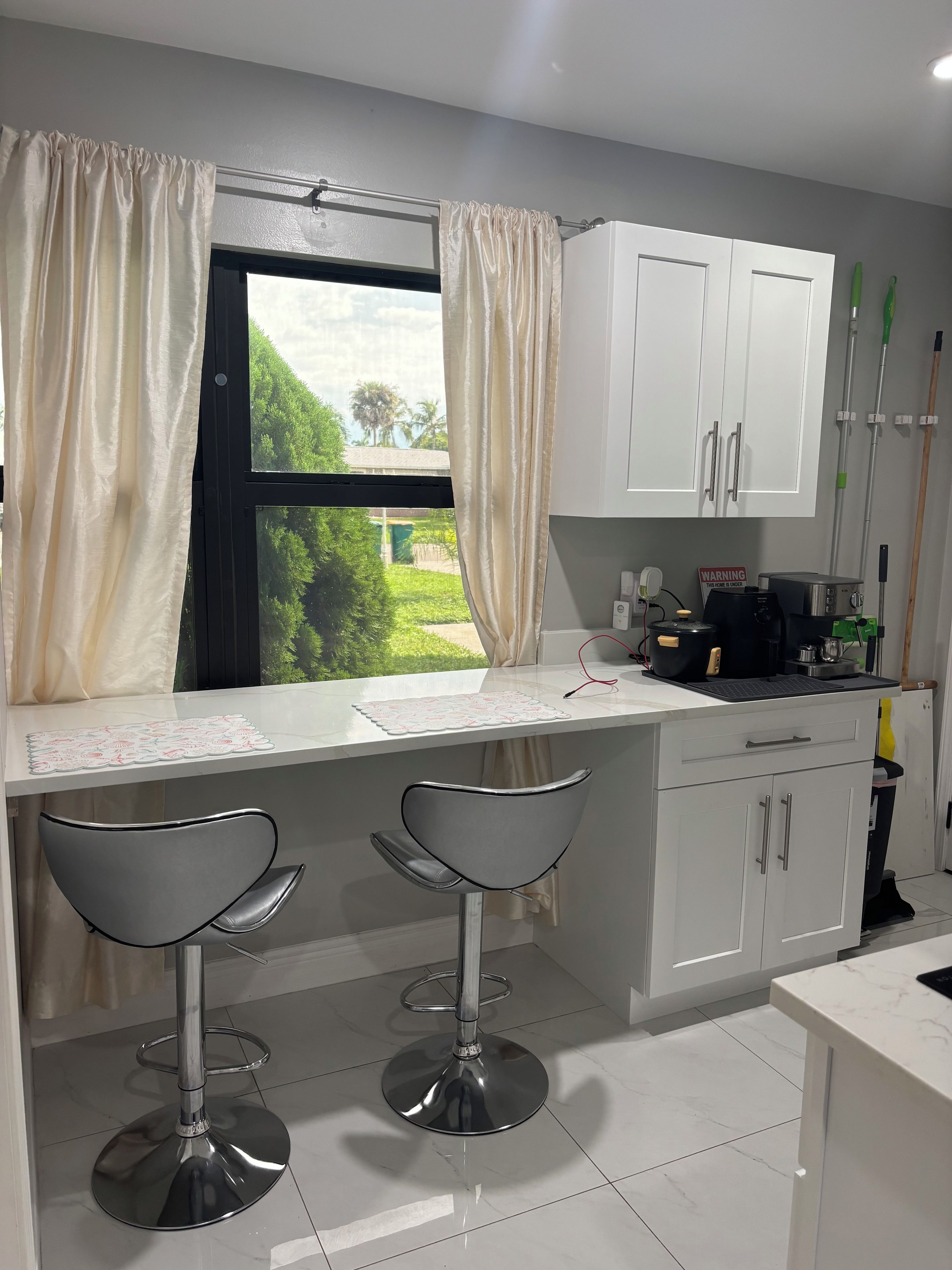 A modern kitchen with a bar area, white cabinets, and a view of greenery outside.