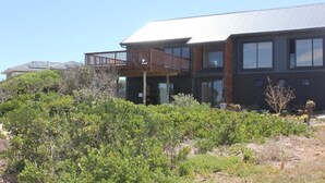 A modern two-story house with a balcony, surrounded by dense shrubbery.
