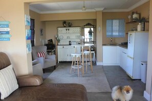 A living room with a brown sofa, a white armchair, and a small table with stools. A dog is in the foreground.