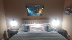 A bedroom with a bed, two bedside tables, a headboard, and a wall-mounted artwork.