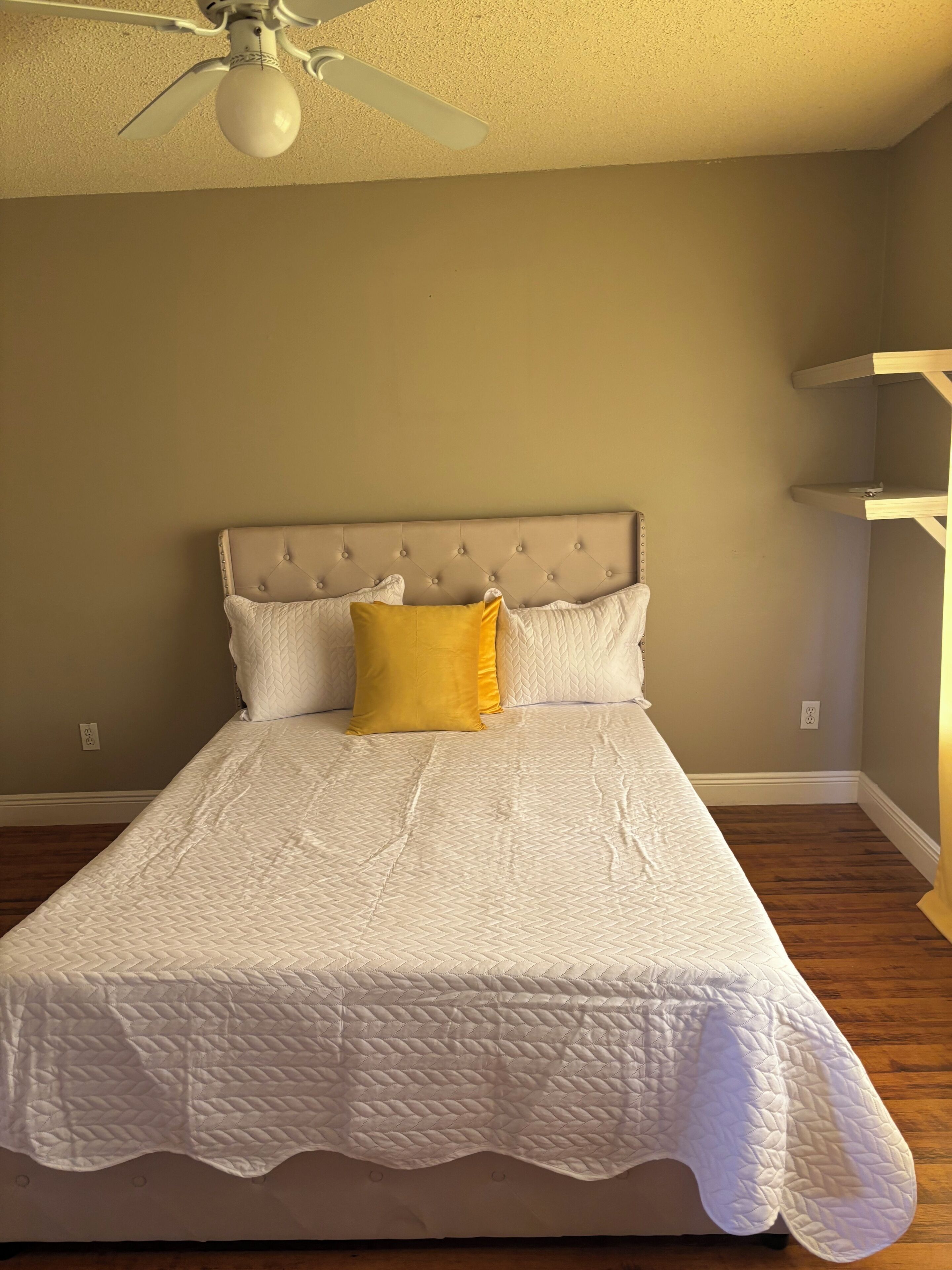 A bed with a tufted headboard, a white quilted bedspread, and a single yellow pillow.