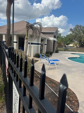 A pool area with lounge chairs, a building with a tiled roof, and a palm tree. - 3-bedroom townhome in fantastic Orlando with cool AC (Orlando)