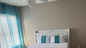 Una camera da letto con un letto, una ventola a soffitto e una finestra con tende.