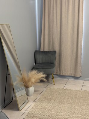A room with a dark grey chair, a standing mirror, a vase with dried pampas grass, and a textured rug on a tiled floor. - 3-bedroom townhome in fantastic Orlando with cool AC (Orlando)