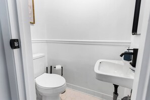 A small, clean bathroom with a toilet, sink, and toilet paper holder. - 2BR 1.5BA Gorgeous Condo Near Hospitals - Shopping (Saint Andrews)