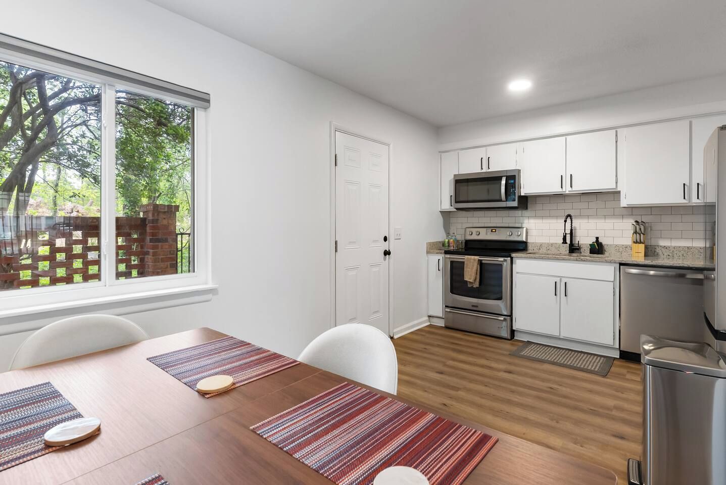 A modern kitchen with white cabinets, stainless steel appliances, and a dining area with a wooden table and chairs.