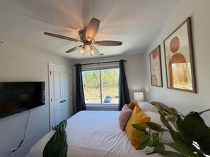 A bedroom with a bed, a ceiling fan, a TV, a window with curtains, and framed artwork on the wall. - 3BR 2.5BA Fort Jackson | Fast WiFi + Parking (Dentsville)