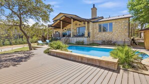 Una casa amb façana de pedra, una piscina i un terrat de fusta.