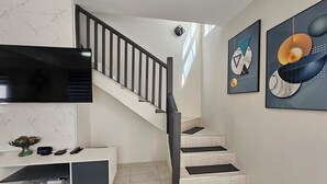 En modern inredning med en trappa, en platt-TV, en vit TV-bänk och abstrakt väggkonst.
