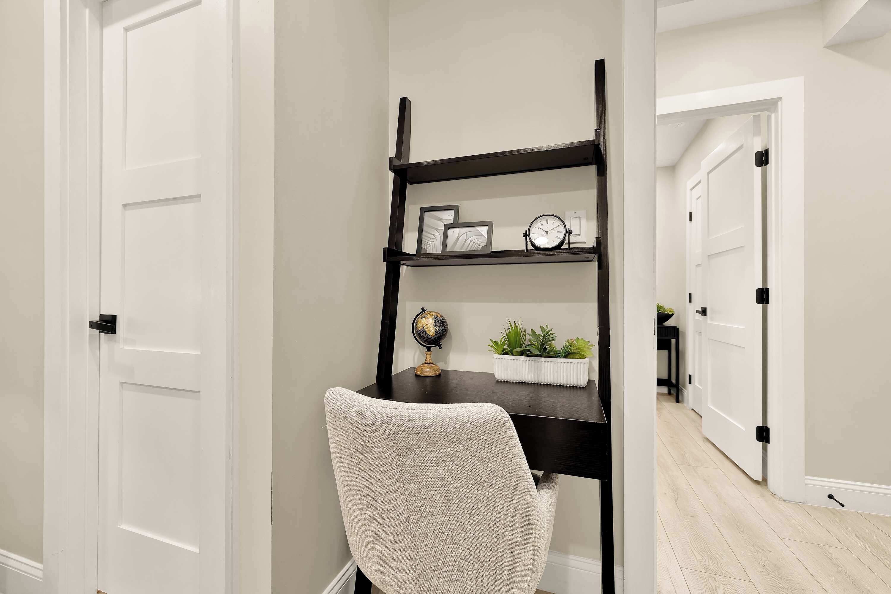 Un espace de travail comprenant un bureau, une chaise et une étagère noire agrémentée d’objets décoratifs.